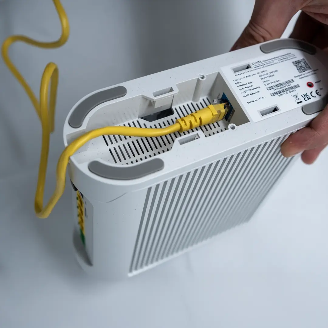 Eine Person hält einen Zyxel-Router in der Hand und hat ein gelbes Netzwerkkabel an den Anschluss auf der Unterseite des Geräts gesteckt.