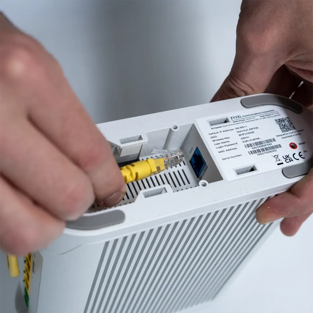 Eine Person steckt ein gelbes Netzwerkkabel in den Anschluss an der Unterseite eines Zyxel-Routers.