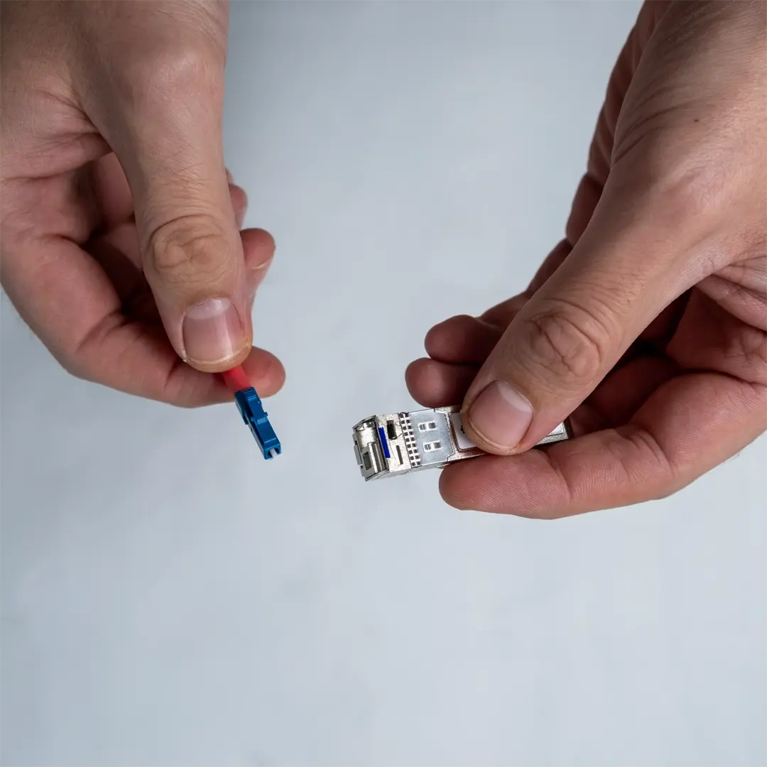 Eine Person hält ein SFP-Modul in der einen Hand und zeigt den Stecker der blauen Glasfaserkabel in der anderen.