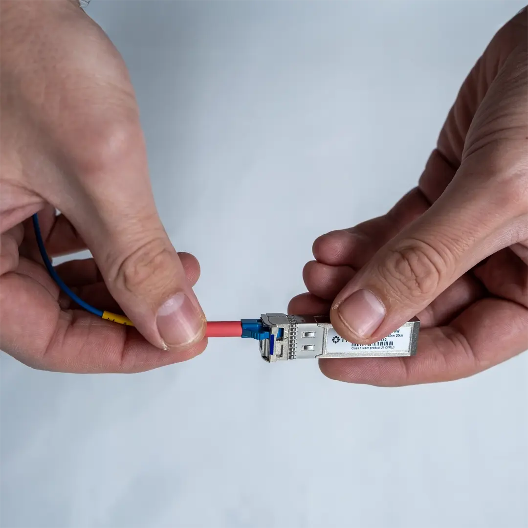 Eine Person schließt ein blaues Glasfaserkabel an ein SFP-Modul an, indem sie den Stecker vorsichtig einführt, bis er einrastet.