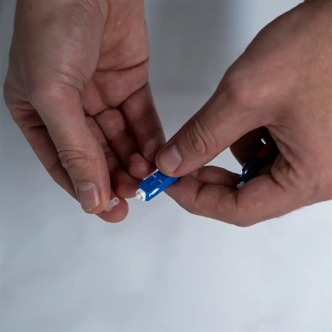 Eine Person entfernt die transparente Schutzkappe vom Ende eines blauen Glasfaserkabels.