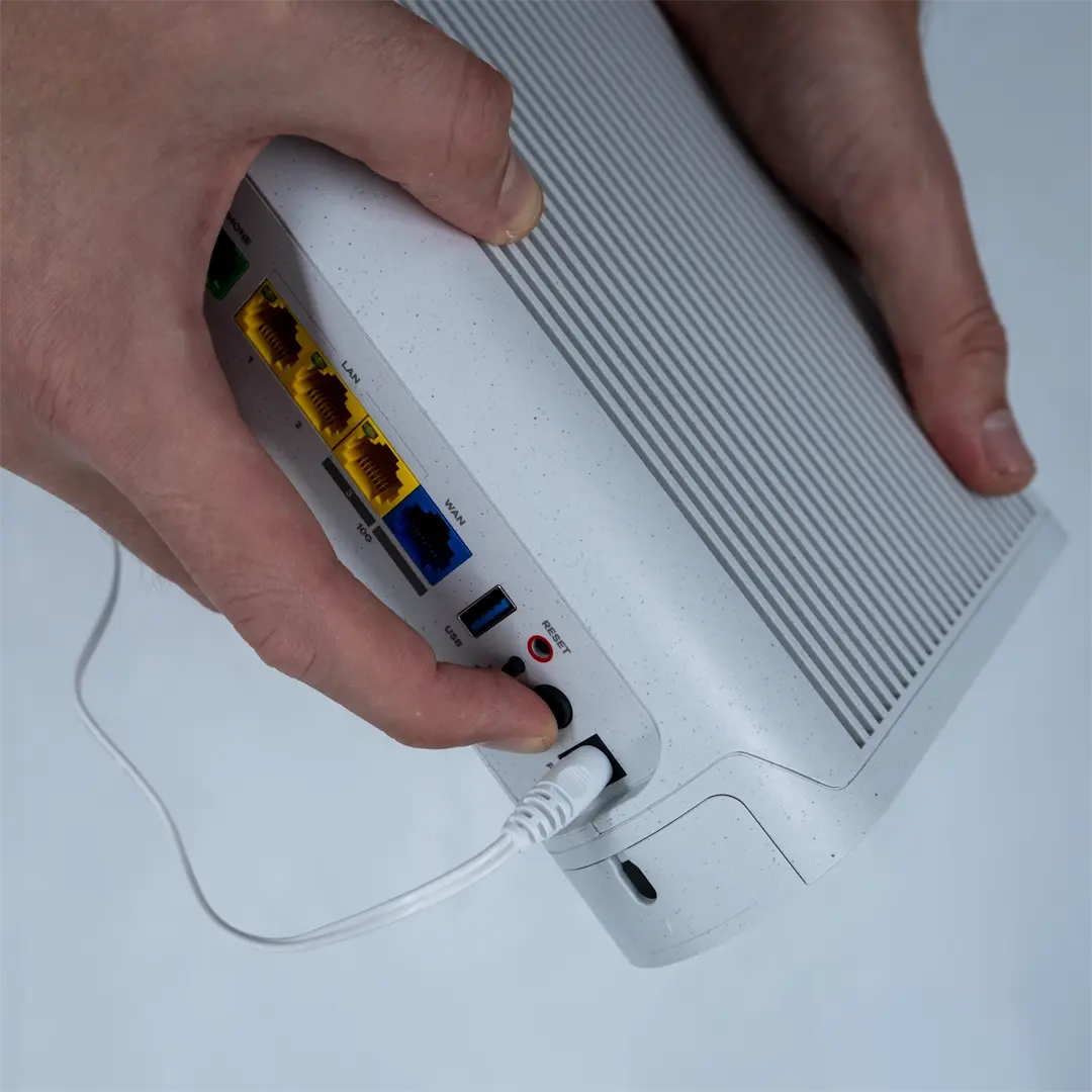 Eine Person drückt den Netzschalter auf der Rückseite eines Routers, nachdem sie das Netzkabel in die Buchse gesteckt hat.